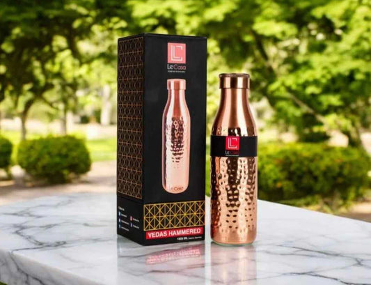 Hammered copper water bottle with Le Casa logo and box on marble table outdoors
